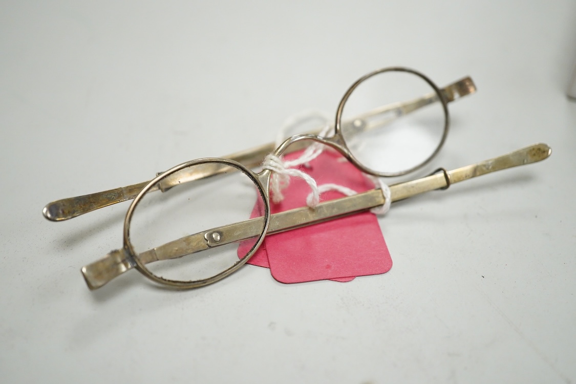 Three pairs of early 19th century base metal slider spectacles, pseudo hallmarks, one also stamped Pebbles, and two pairs of similar temple spectacles, the pair with turn pin sides also stamped pebbles, the pair with obl